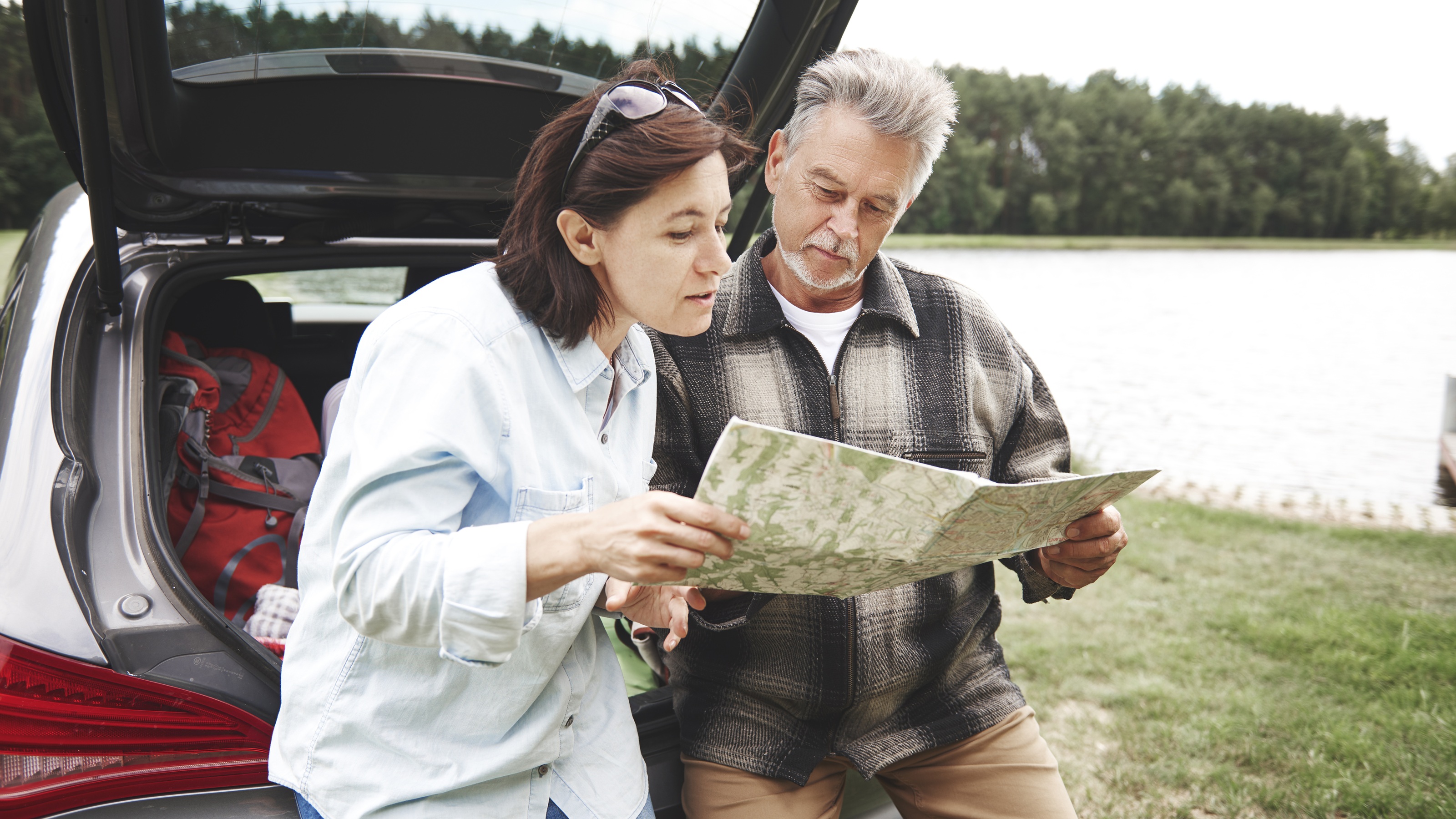 An older couple look at a map together outside their SUV.