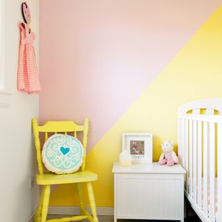 A children's room with one wall painted in two tones divided diagonally, with the top in pink and bottom in yellow