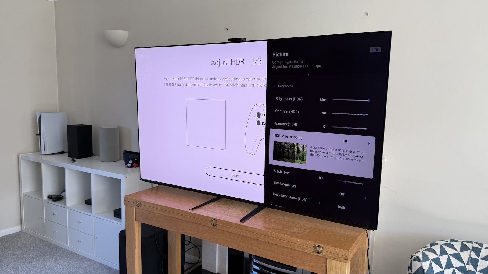 The 65-inch Sony A95L pictured on a wooden table in a living room. On the screen is the PS5 Adjust HDR menus