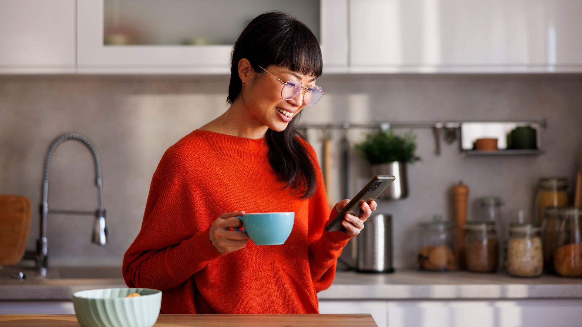 Woman standing in kitchen looking at phone