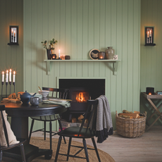 Cosy green panelled dining room with lit log burner, black dining table and chairs and candles.