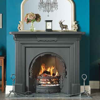 black georgian style fireplace in blue living room with statement mirror above