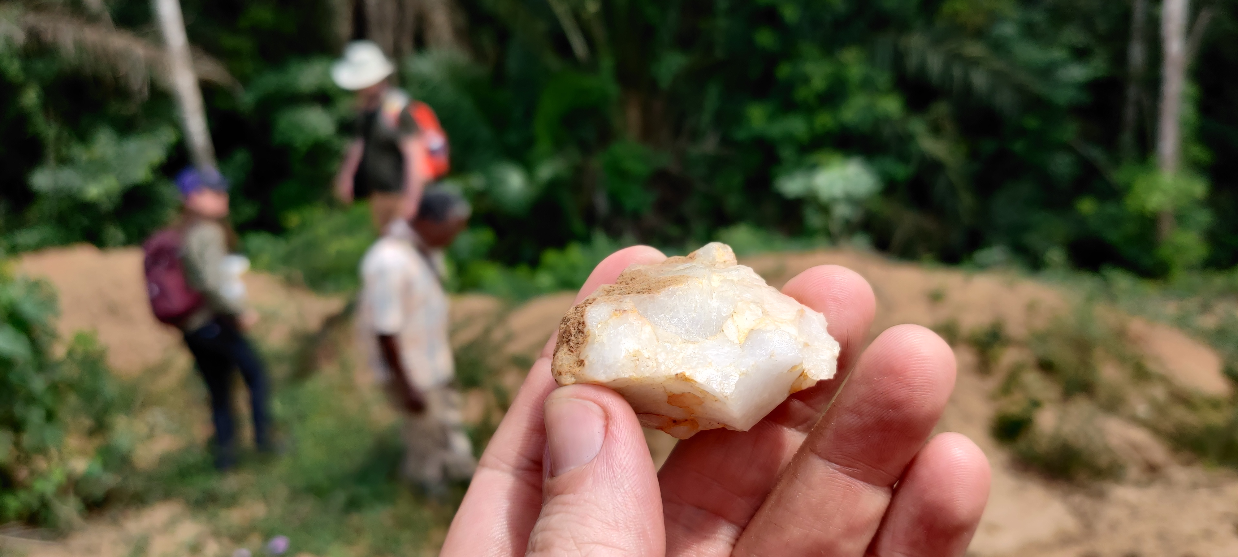 Small quartz tool held in hand with archaeologists working in the background