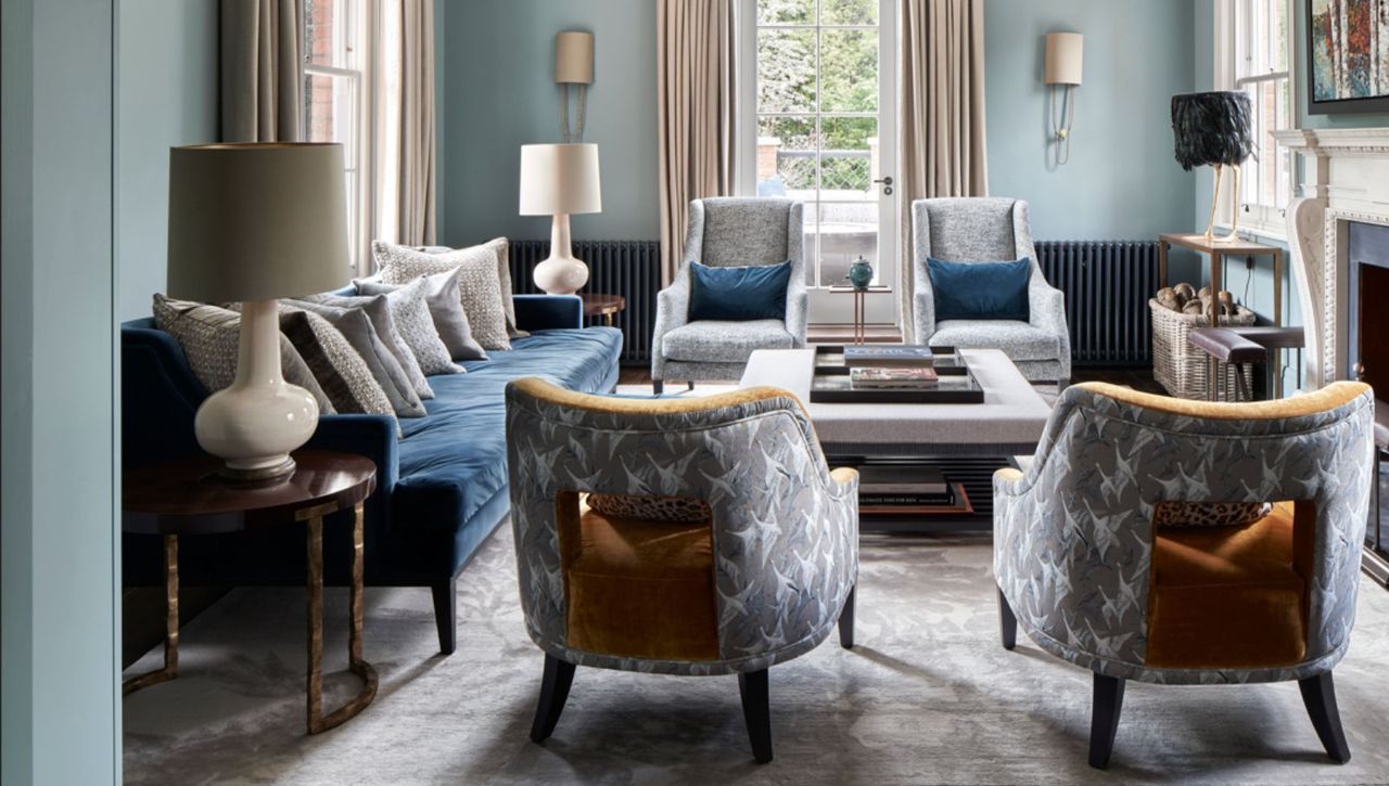  Living room with blue walls, grey rug, ornate fireplace with lit fire, grey carpet and upholstery, and grey curtains. 