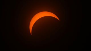 A partial solar eclipse showing the sun as a narrow red crescent