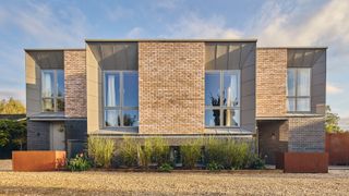 brick and zinc clad modern house with large windows and copper colour planters along front of house