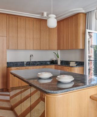 Light-colored wooden kitchen cabinets with a round wooden island and mirrored cabinet fronts and green marble countertops