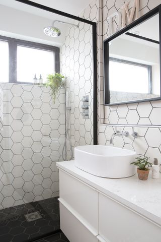 Monochrome bathroom with industrial black-framed walk-in shower, hexagonal wall tiles and a white vanity unit and sink