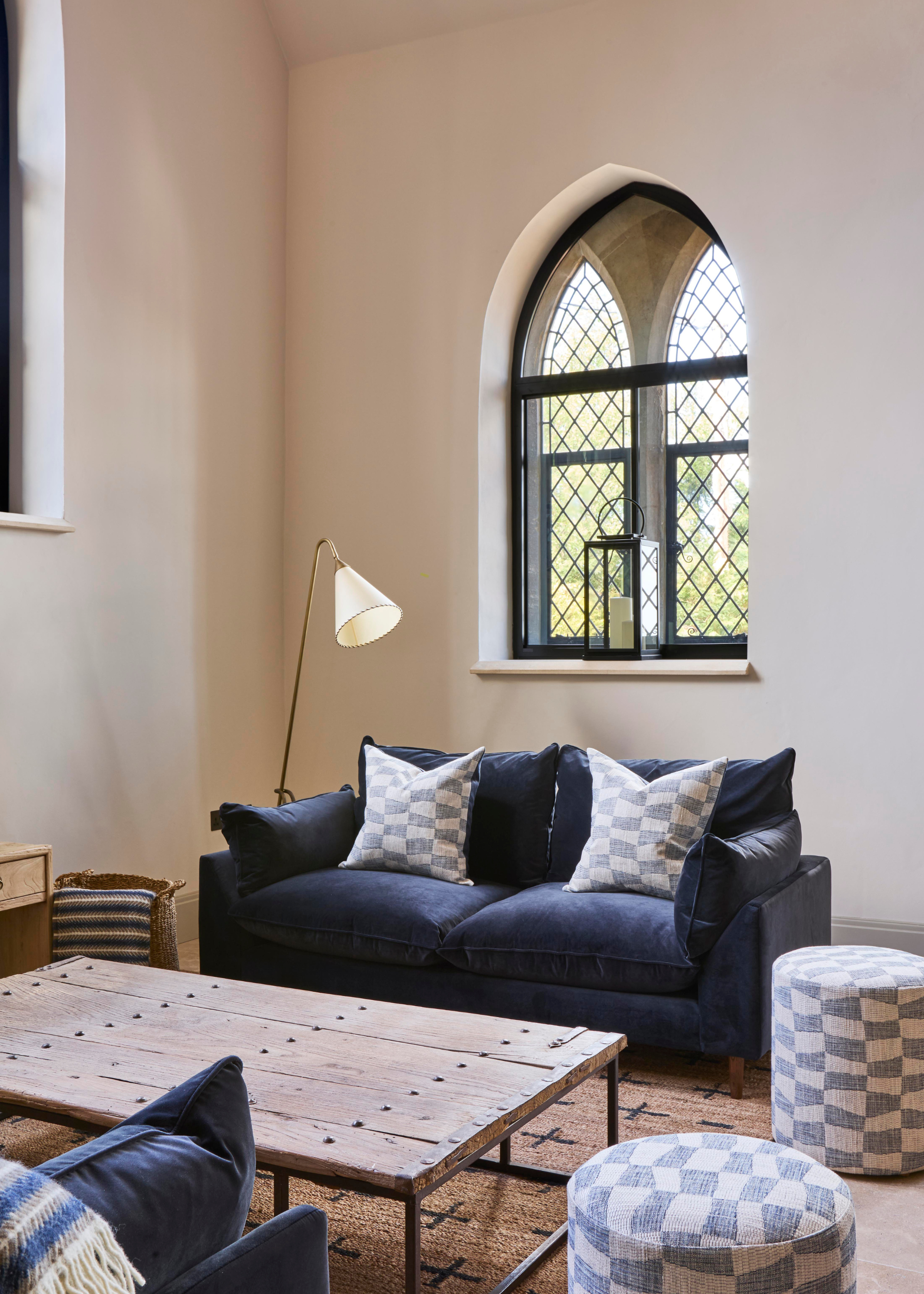 converted chapel living room with blue velvet sofa and checkered poufs