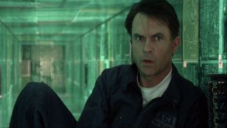 Sam Neill sits in a computer corridor with an expression of concern in Event Horizon.