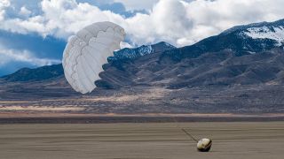 a cone-shaped capsule lies on the desert floor with a parachute billowing in the wind above it