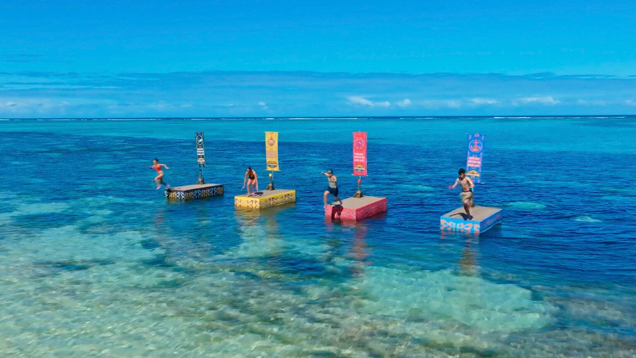 Survivor contestants stand on platforms as camera crews film during a Final Four challenge in Season 49. 