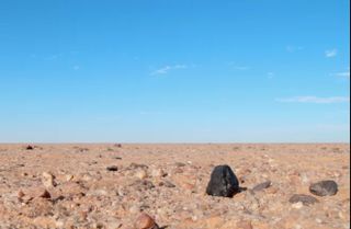 The black fragment of Almahata Sitta meteorite No.number 15 appears stark against the lighter-colored rocks of the Nubian Desert in northern Sudan.