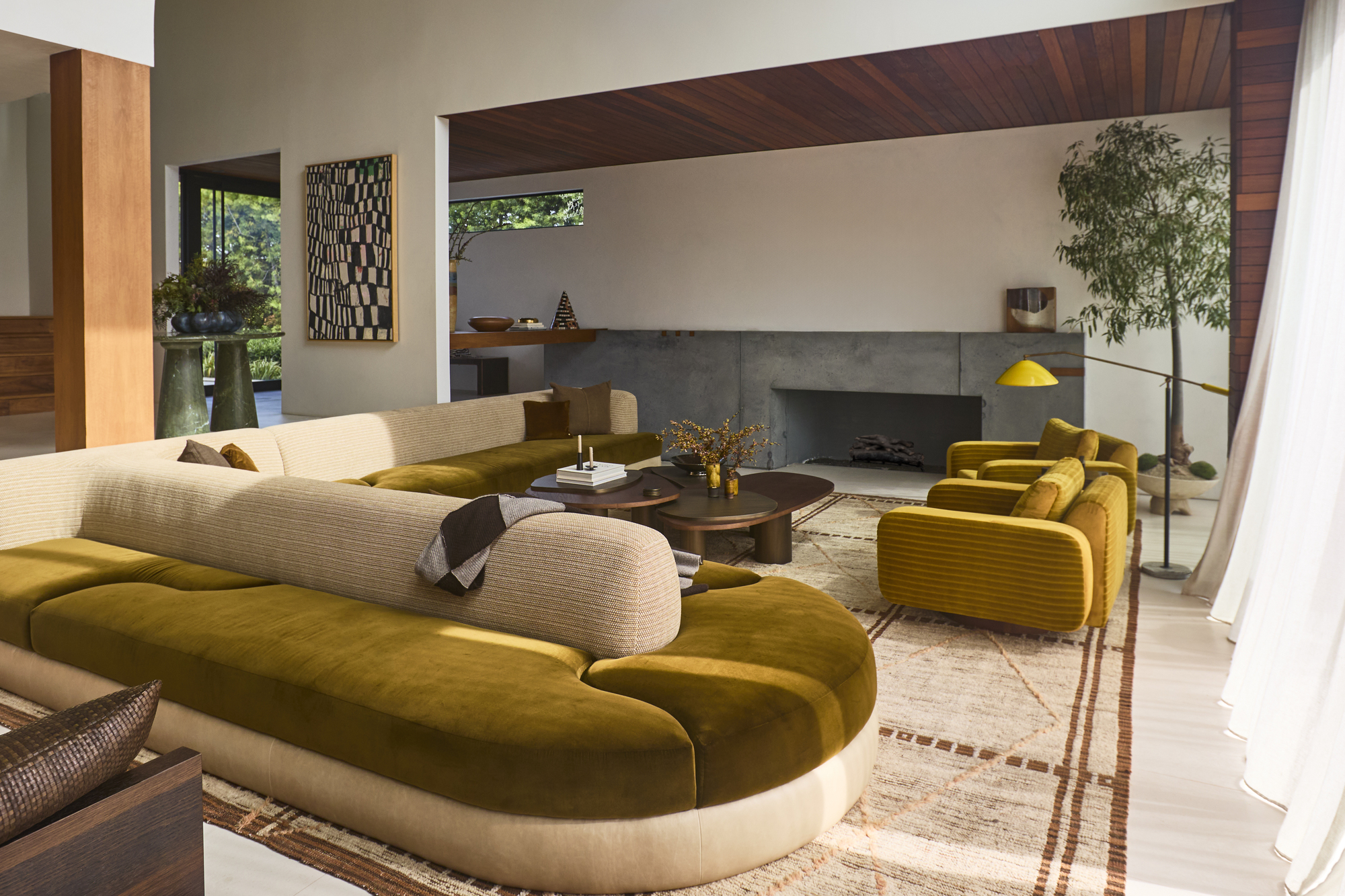 modern living room with floating, double-sided curved sofa with green mohair seats, yellow armchairs, nesting coffee table, built-in fireplace and patterned beige rug with timber paneling on the wall and ceiling