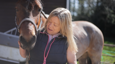 A lady looking at her pony who is stood alongside wearing a headcollar.