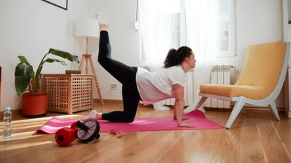 A woman performing a donkey kick as part of a home workout in her living room