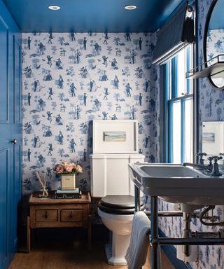 cabinets on left, blue woodwork and ceiling, side table with flowers, basin with towel storage, blind