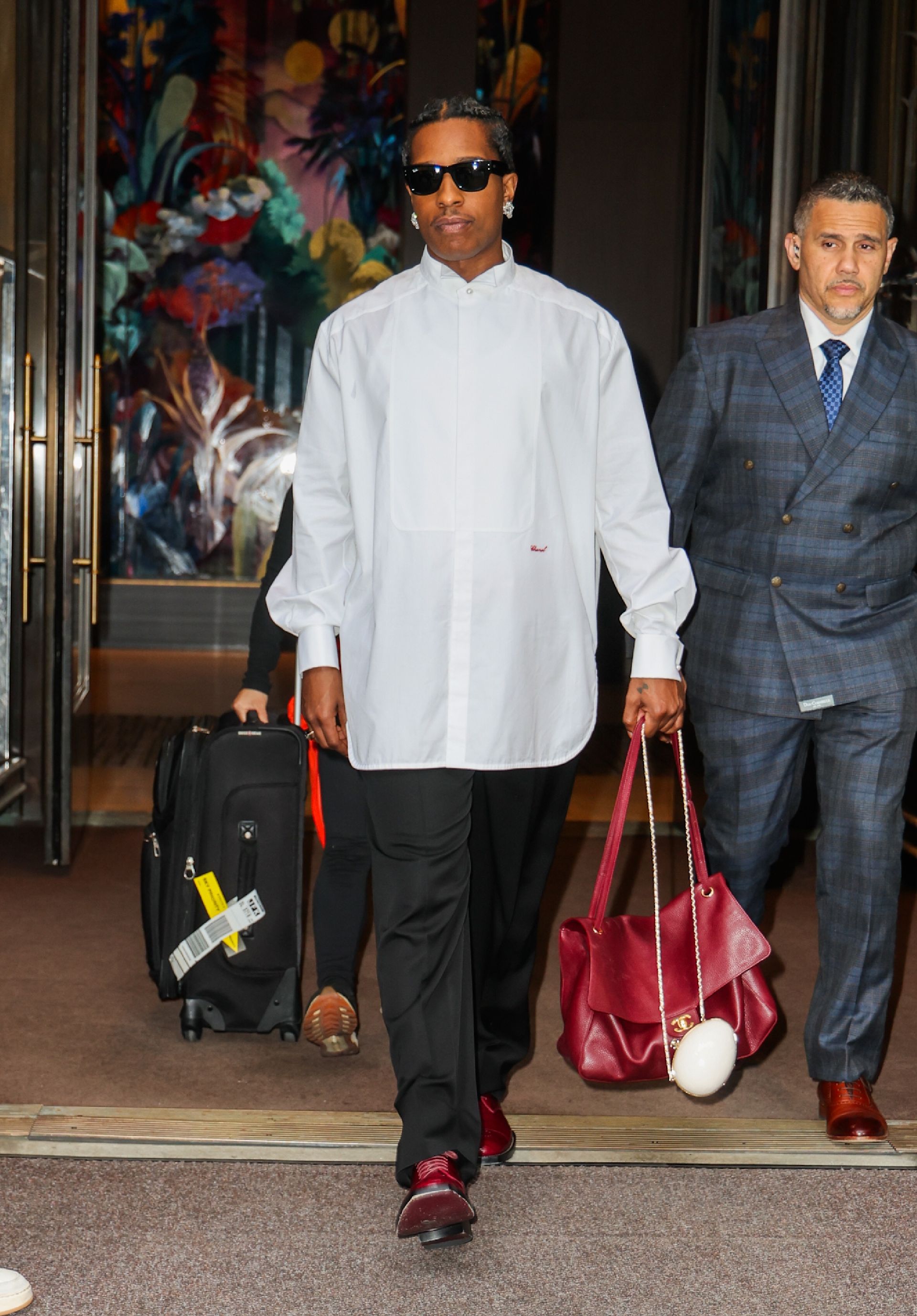 Asap Rocky steps outside wearing an red Chanel bag with a white shirt and black trousers.