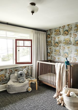 nursery with dinosaur wallpaper, wooden crib, textured gray rug, gray chair, stool, basket with toys, cream drapes