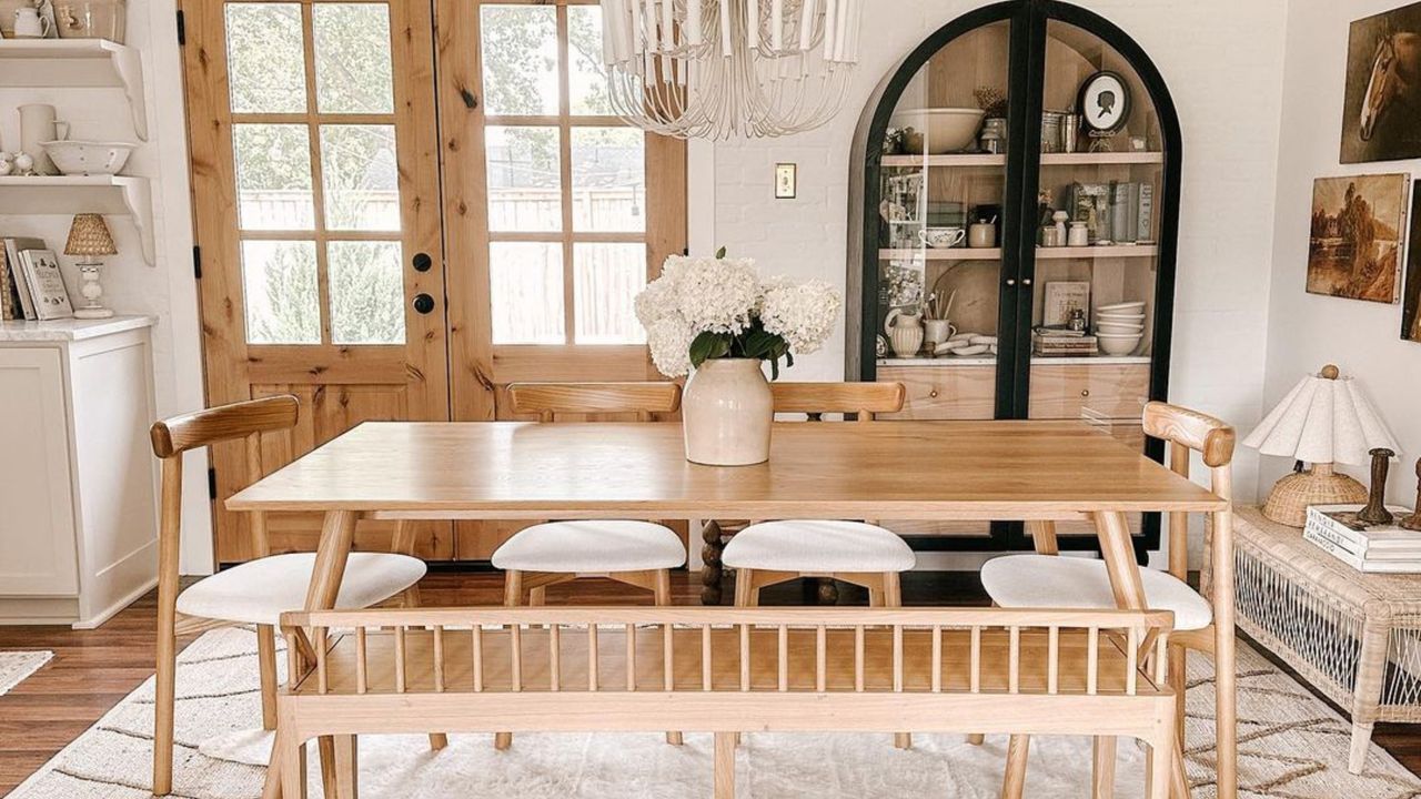 Neutral dining room with wooden table, white flower centerpiece, and black cabinet