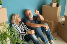 T8BENR Mature couple sitting on floor near boxes indoors. Moving into new house