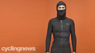 Writer wearing Assos Equipe RS Mid Layer, with hood up, facing the camera in front of an orange background