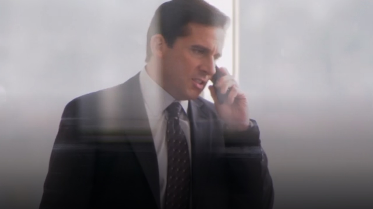 Michael está enojado por teléfono (se muestra a través de una ventana) en la oficina.