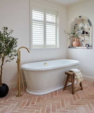 White bathroom with terracotta floor tiles and a freestanding bath