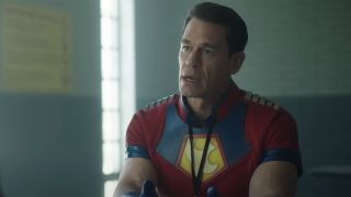 John Cena with a visitor badge on sitting at a prison table in Peacemaker Season 2