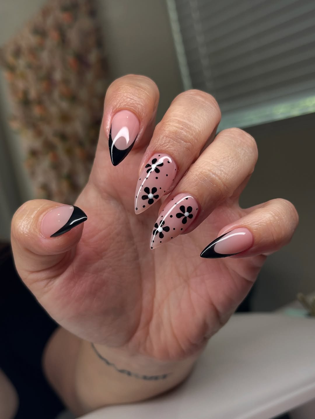 a person wearing sharp nails with black tips and black flowers on the middle fingers