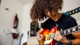 Boy with long hair plays a sunburst electric guitar