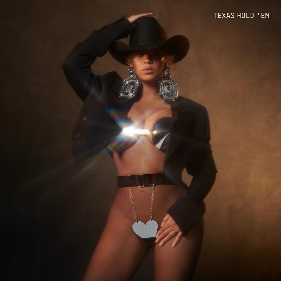 a woman (beyonce) poses in a black cowboy hat, a black bolero, a silver bra top and a silver bikini top with a black waistband, on the cover of the single 