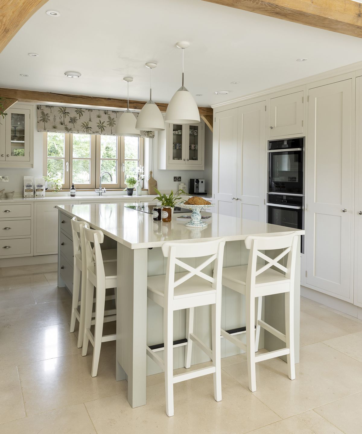 A neutral kitchen with light coloured flooring and cabinetry with central island and exposed beams