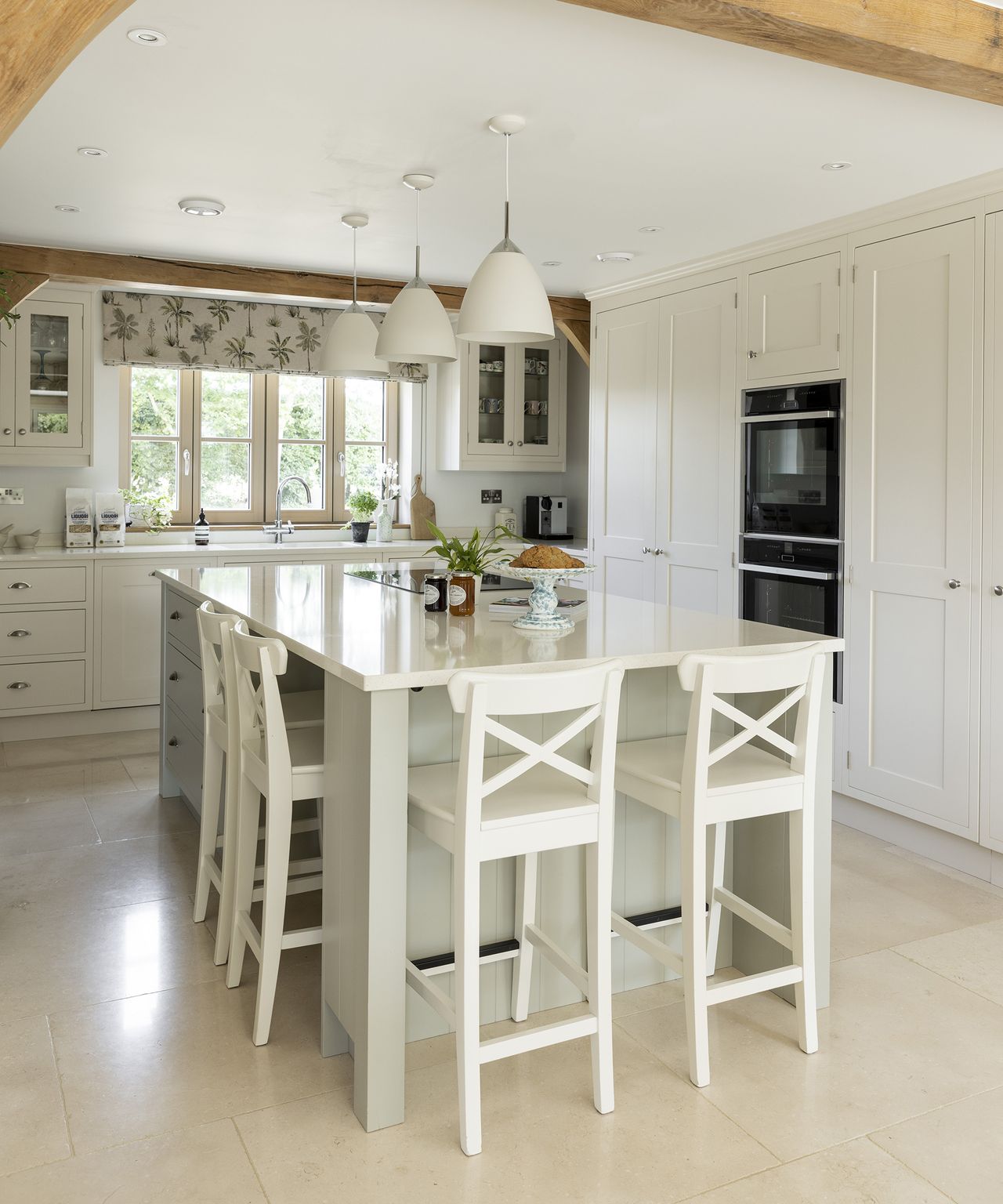 A neutral kitchen with light coloured flooring and cabinetry with central island and exposed beams