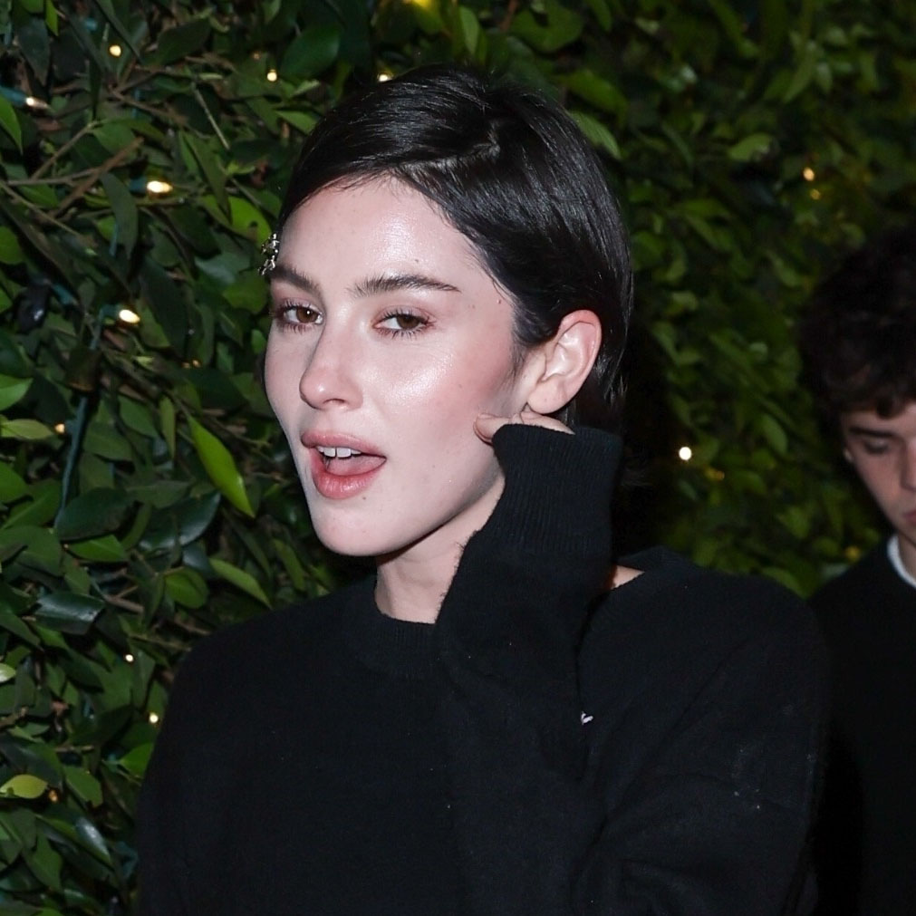 Gracie Abrams wearing a black sweatshirt and black pants with a red clutch 