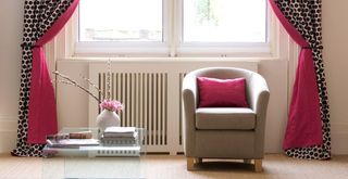 Cream living room with red lined patterned curtains with tie backs with a tub armchair