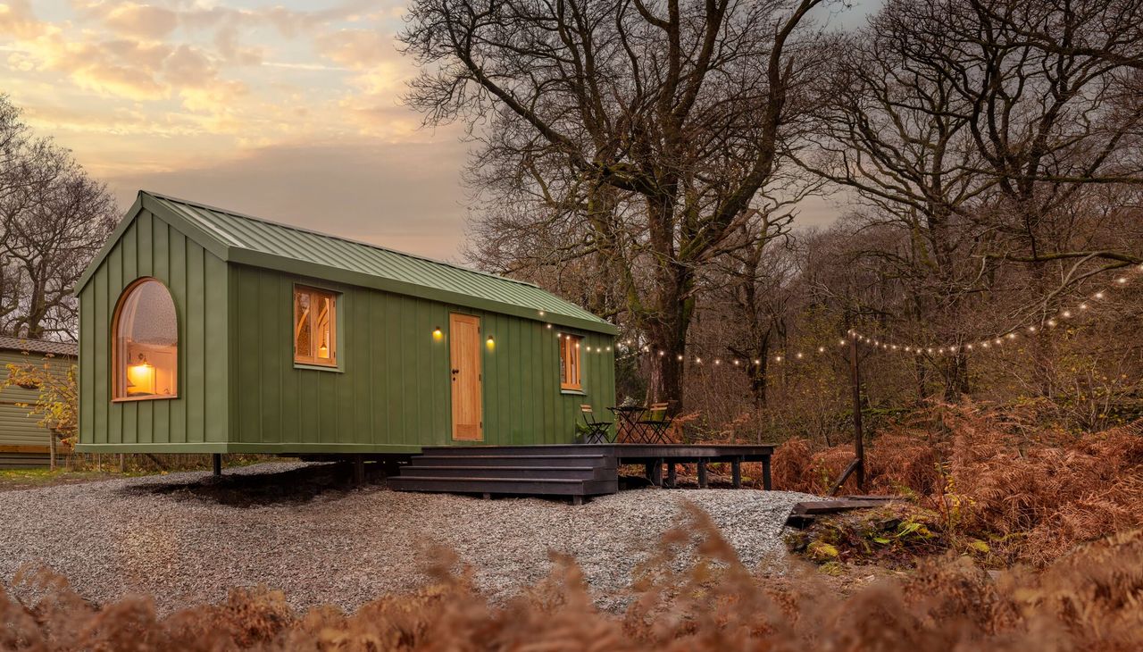 A green caravan with the lights on seen amongst woodland