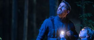 Ryan Reynolds and Walker Scobell looking towards the sky in a blue lit forest in The Adam Project.