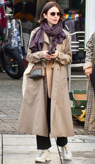 Lily Collins wearing a trench coat with Salomon sneakers.