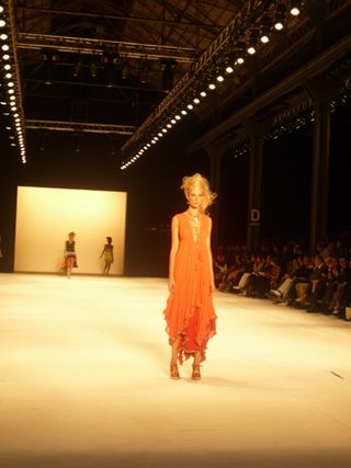 Model on runway wearing a long, layered orange dress