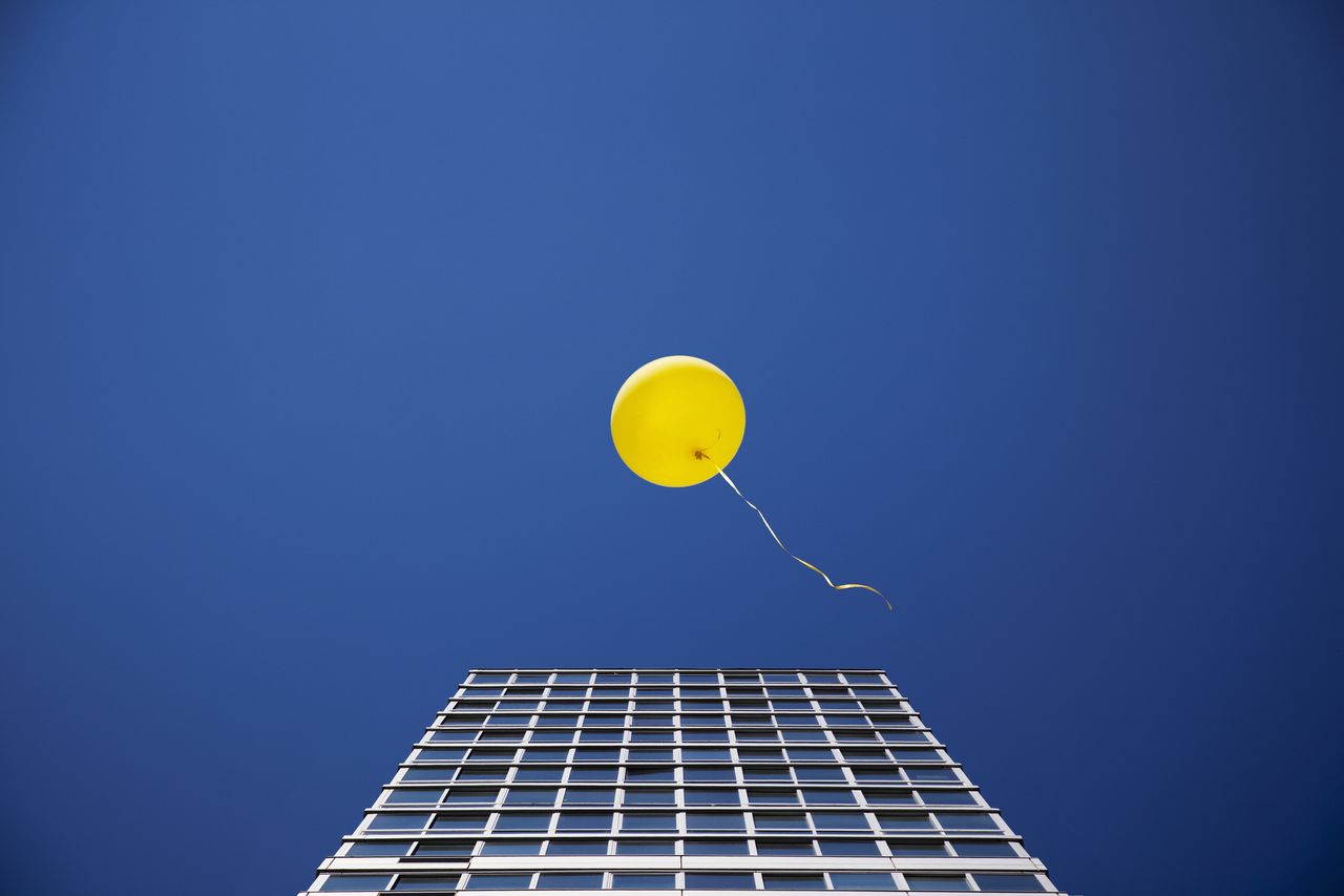 yellow balloon against blue sky with skyscraper