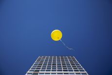 yellow balloon against blue sky with skyscraper