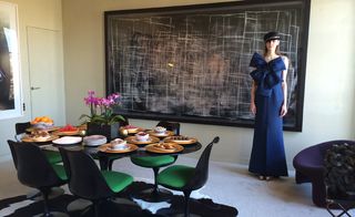 An apartment dining room with table set and woman stood next to the huge painting filling the wall