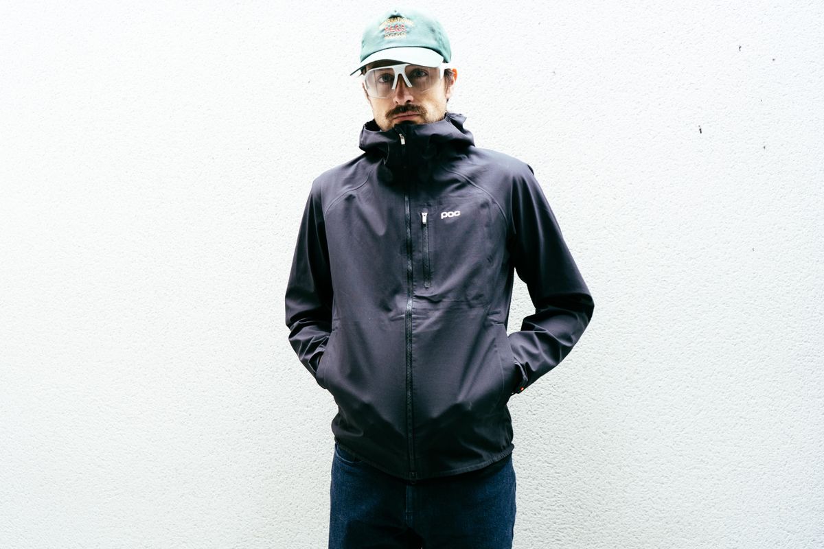 A man in a black rain jacket against a white wall