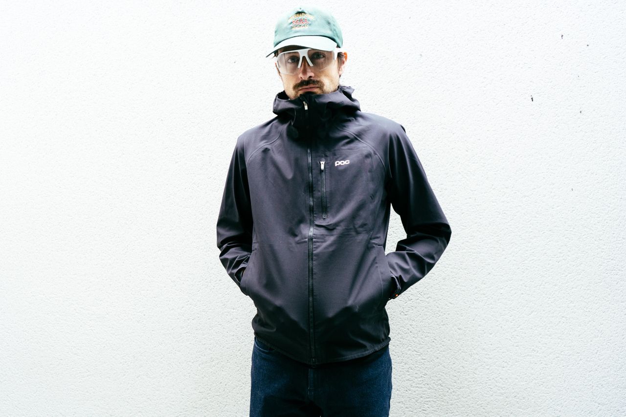 A man in a black rain jacket against a white wall