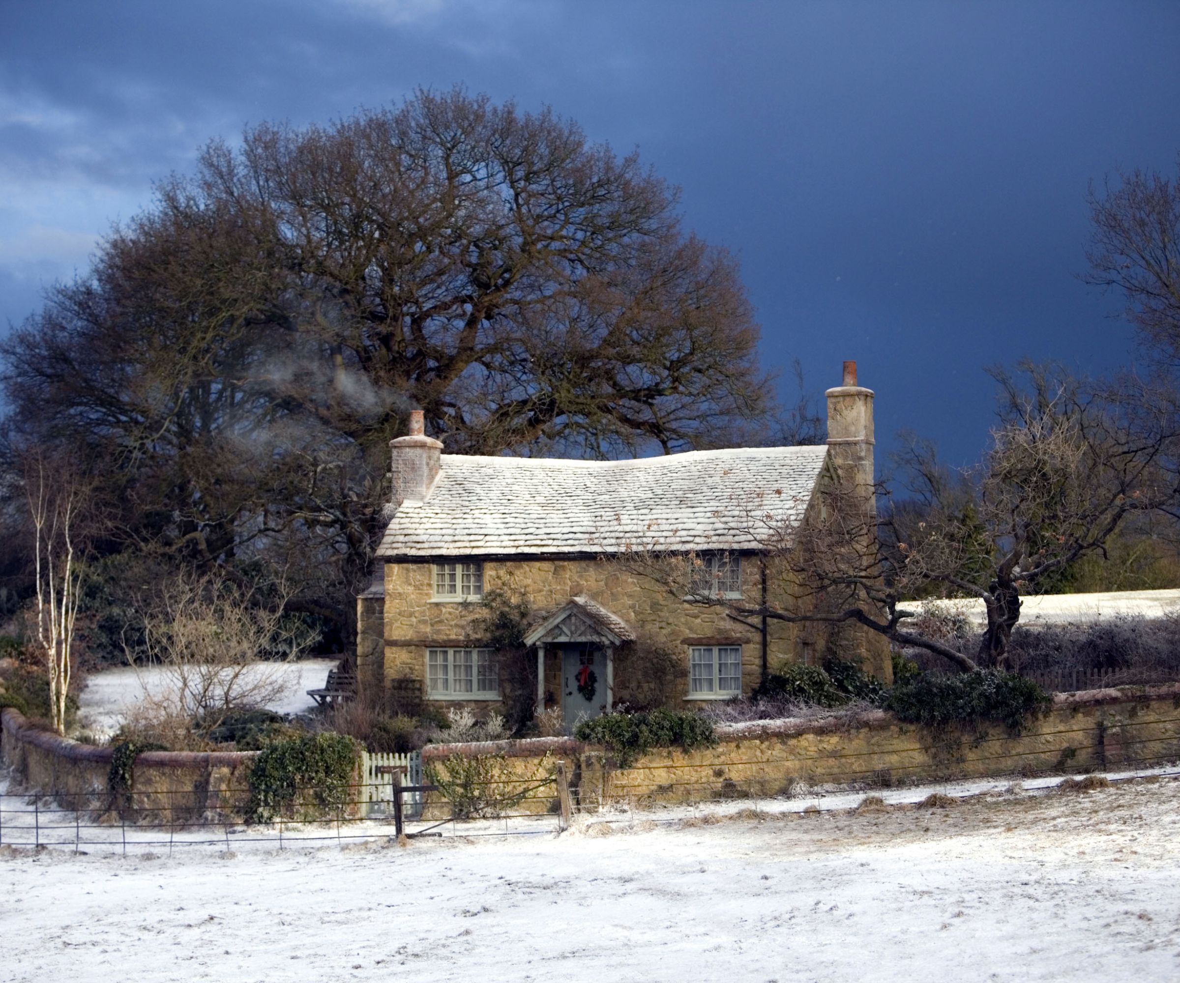 the exterior of 'rose cottage' from The Holiday 2006 in the rural english countryside made from cotswold stone, surrounded by trees and with a covering of snow