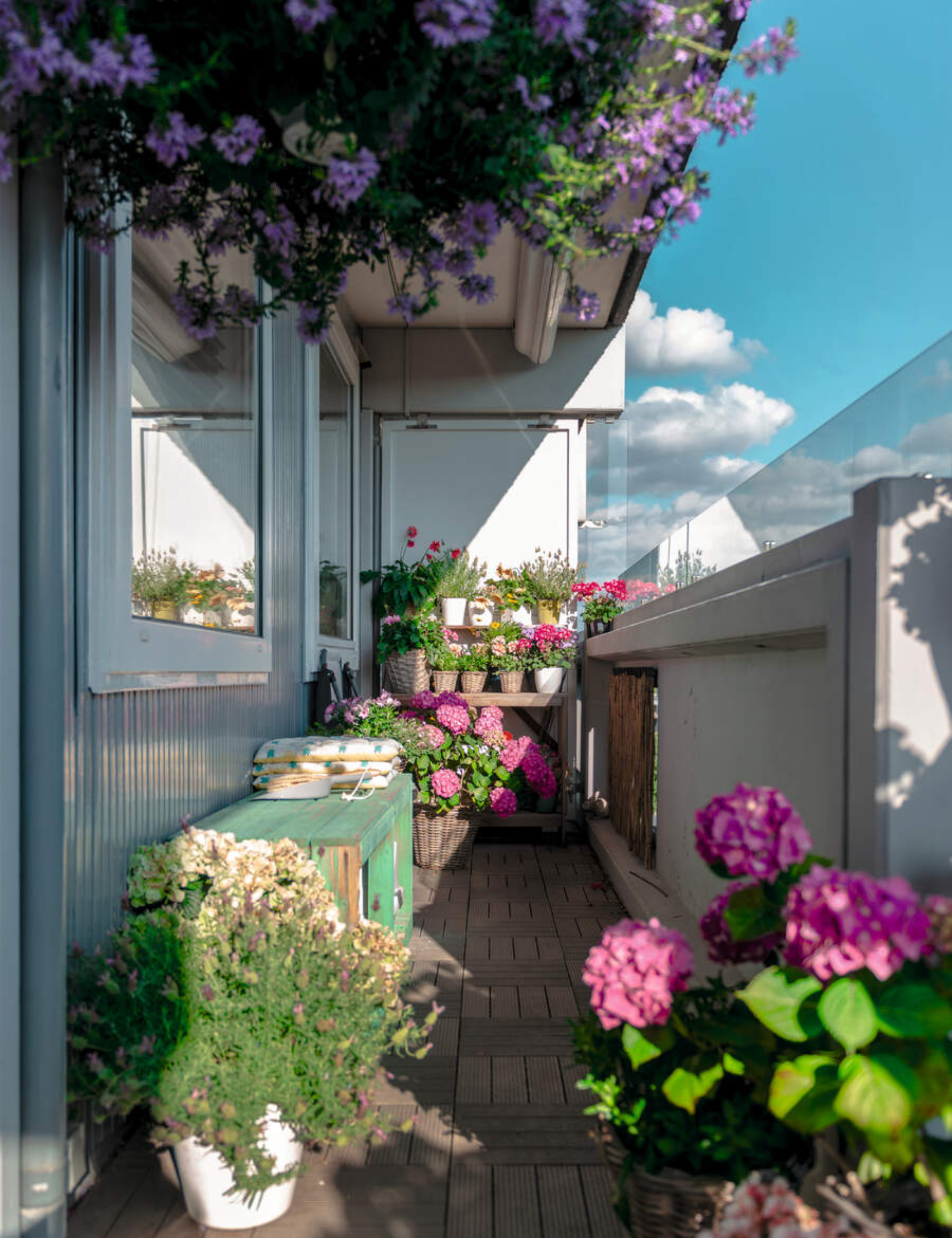 Flower-filled balcony garden with brick floors overlooking a bright blue sky