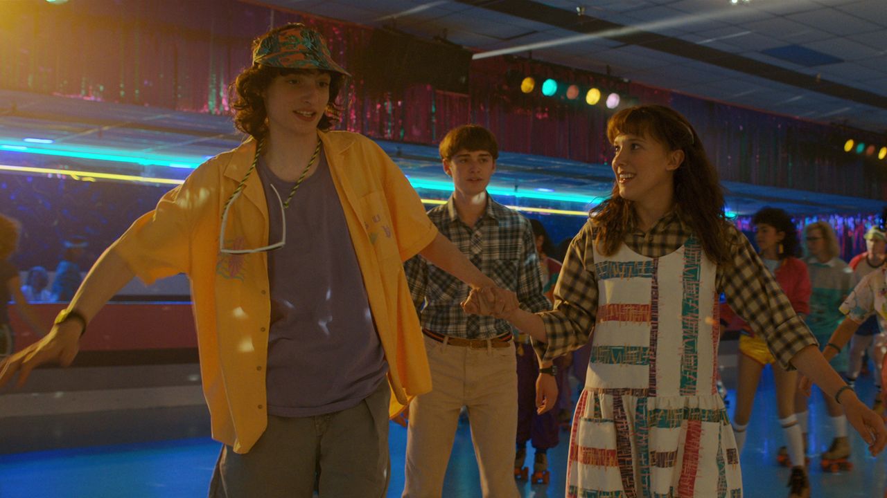Finn Wolfhard and Millie Bobby Brown hold hands while roller skating in Stranger Things