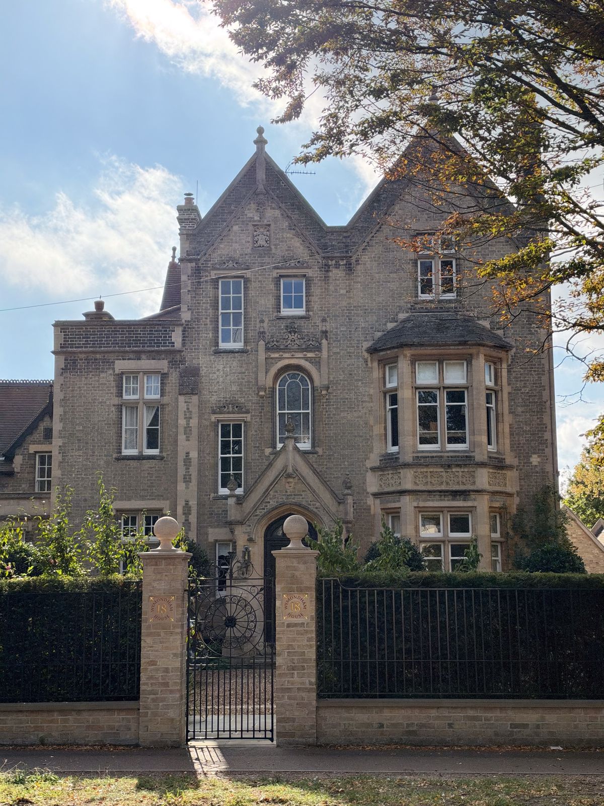 Ornate historic stone house with bay windows, steep gables, and a gated front garden in bright sunlight.