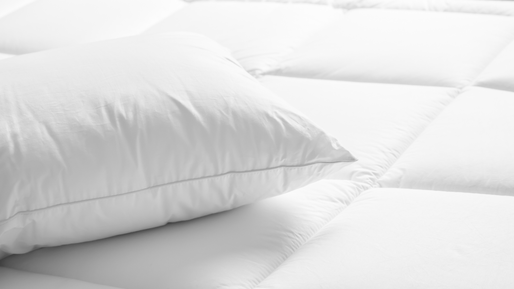A white quilted mattress topper with a white pillow placed on top of it